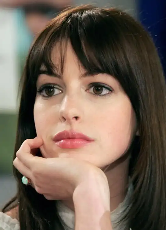 Anne Hathaway soft wispy full bangs grazing the eyebrows, blending into sleek long hair for an elegant and refined hairstyle.