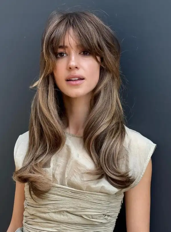 Dakota Johnson curtain bangs parted in the center, softly framing the face and blending into long layered hair for a modern, effortless look.