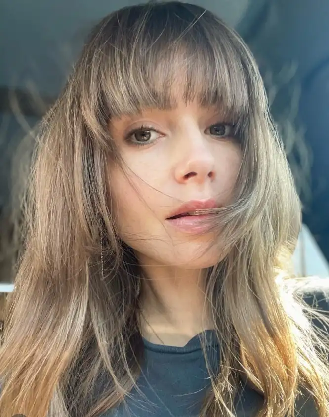 Lily Collins soft feathered bangs paired with long layered hair, creating a natural, face-framing hairstyle with light movement and volume.