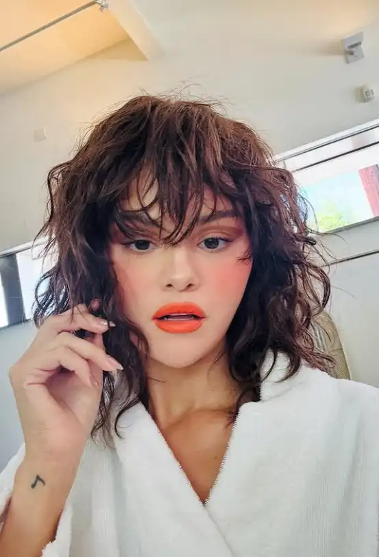 Selena Gomez wispy textured bangs paired with soft waves, creating a relaxed, tousled hairstyle with natural movement and light fringe.