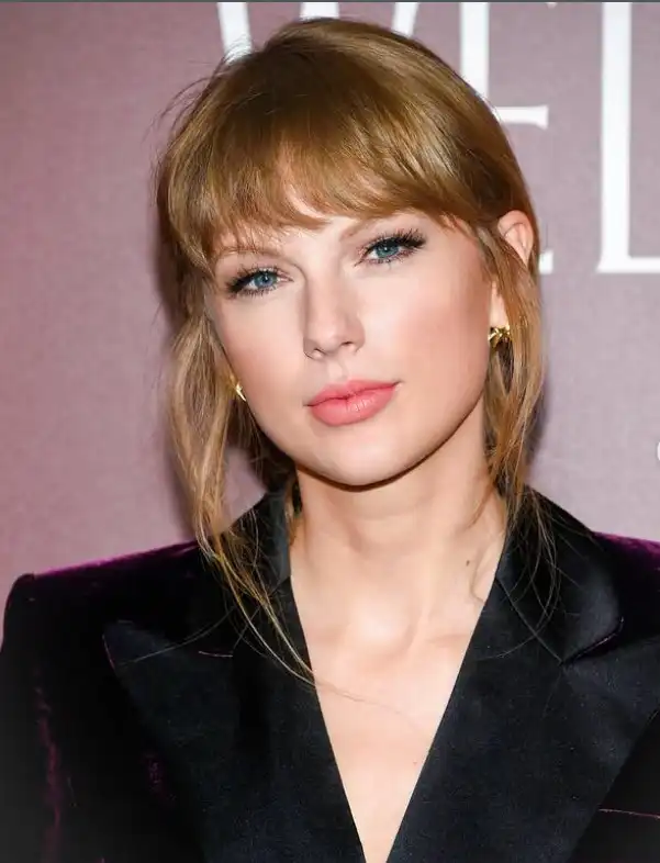 Soft wispy bangs on Taylor Swift with natural movement, lightly covering the forehead and blending into long hair for a youthful, polished everyday hairstyle.
