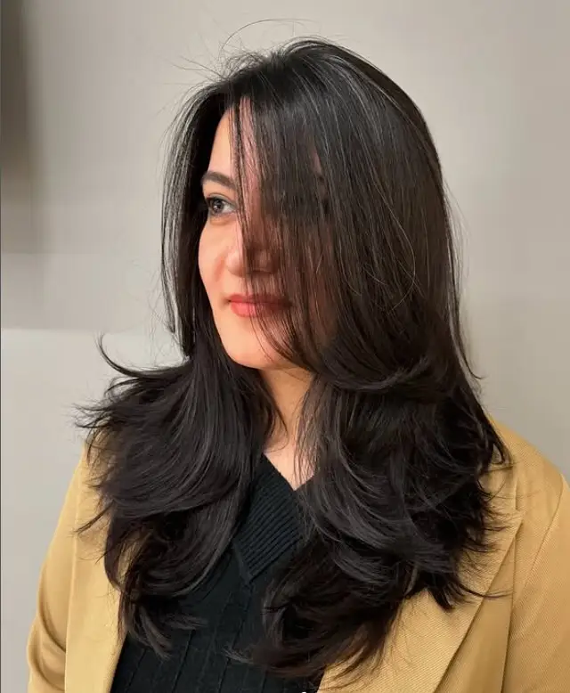 Voluminous layered hairstyle with side bangs for round face full look