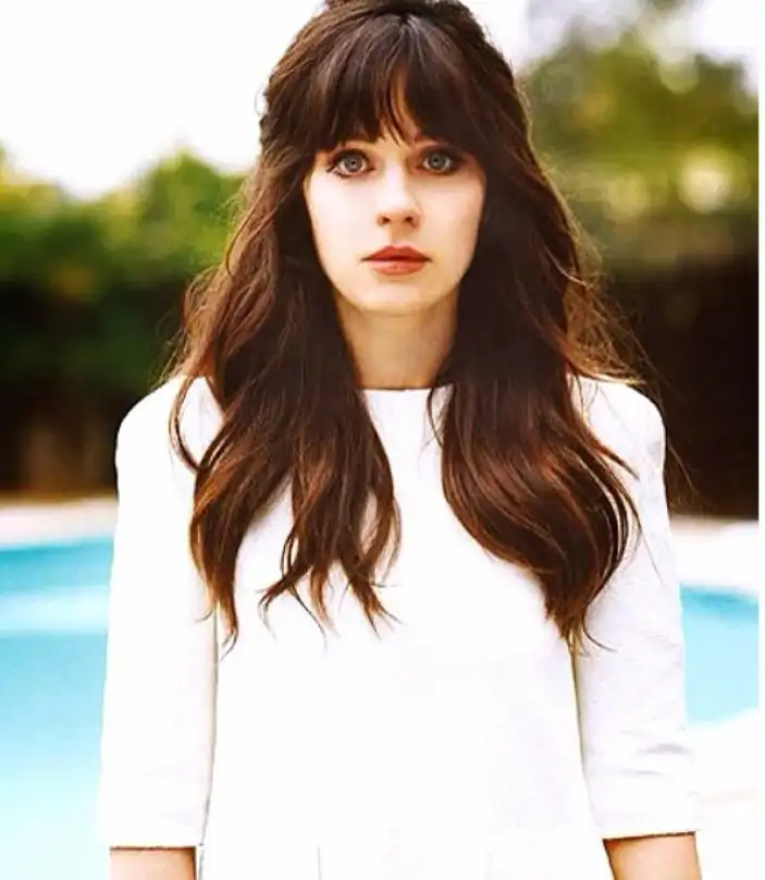 Zooey Deschanel full fringe bangs covering the forehead completely, creating a bold, iconic hairstyle with strong face-framing definition.