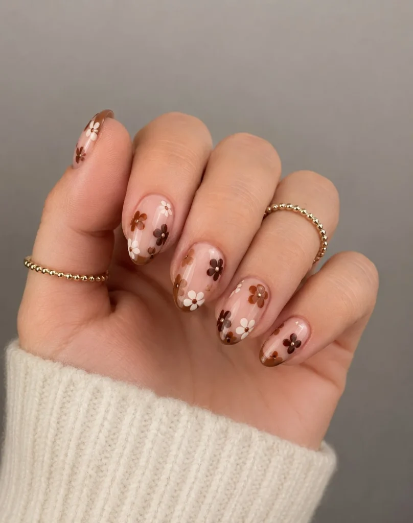 Short brown almond nails with soft floral accent designs on a neutral brown base, simple feminine nail art with minimal floral details on one or two nails