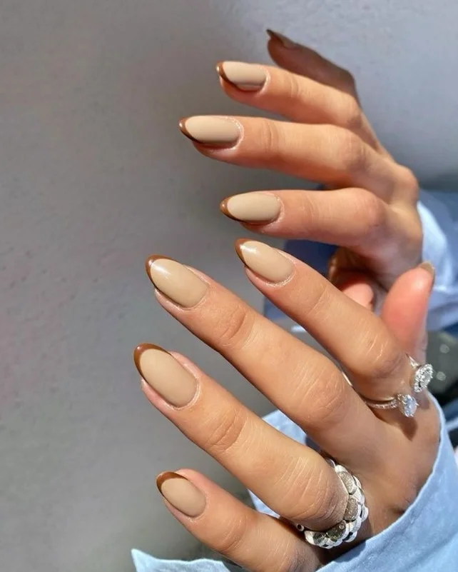 Almond-shaped nails with light brown French tips on a natural nude base.
