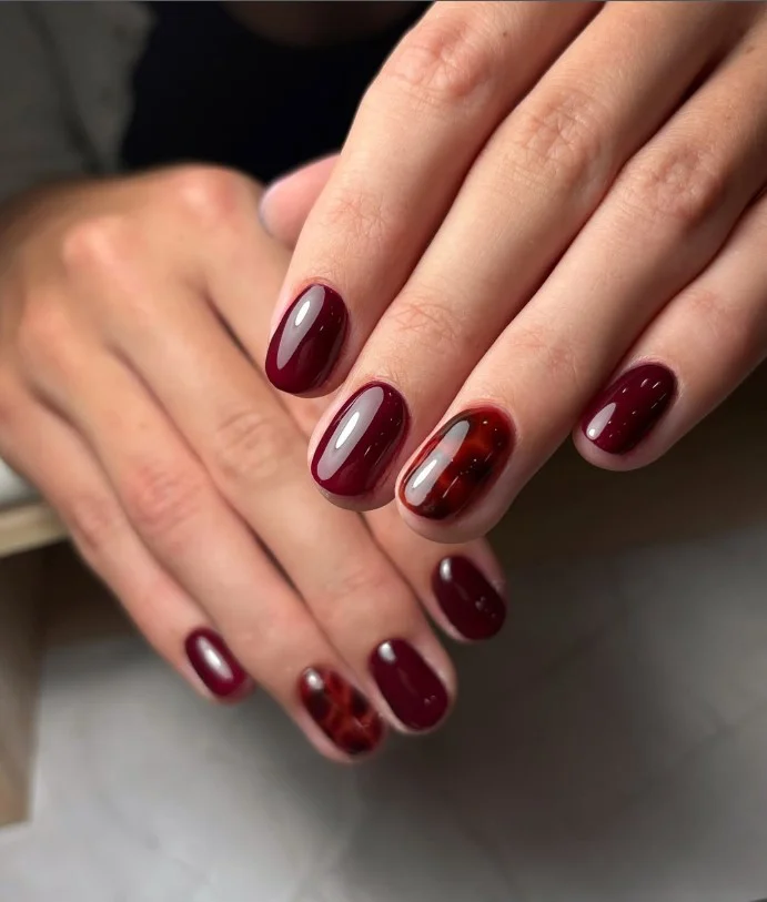 Burgundy fall nail designs combined with tortoiseshell accent nails for a luxurious autumn-inspired look.