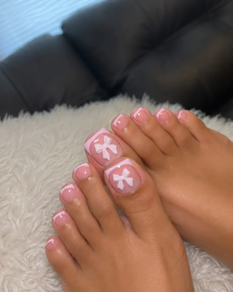 Coquette toe nail designs featuring delicate bow accents on a glossy pastel pedicure.