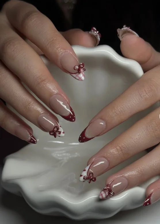 Cute coquette red nail designs with elegant 3D ribbon accents on a glossy cherry red manicure.