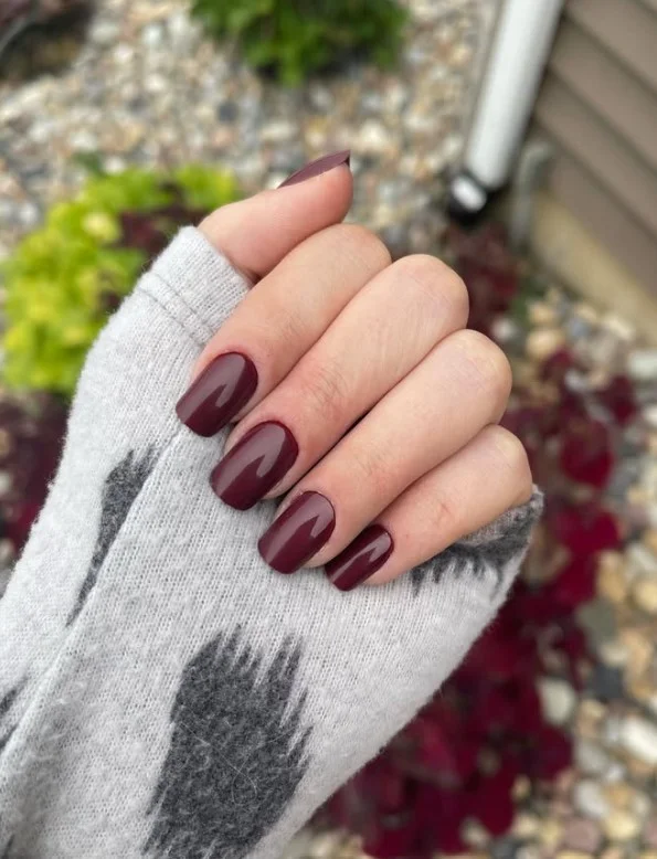 Deep plum nails creating a stylish contrast with an emerald green dress.