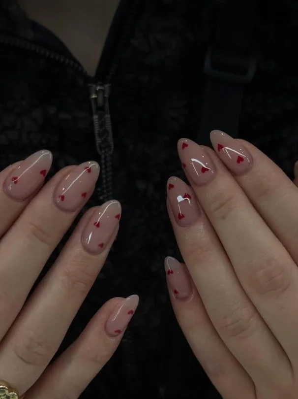 Long acrylic nails featuring tiny heart nail art on a glossy nude base for a romantic look.