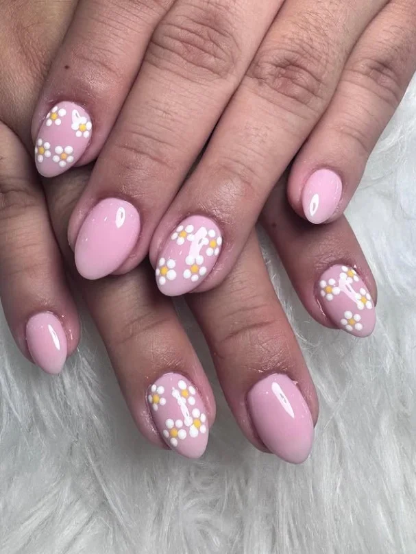 Pink floral nail designs featuring delicate white daisy artwork on a glossy pastel pink base.