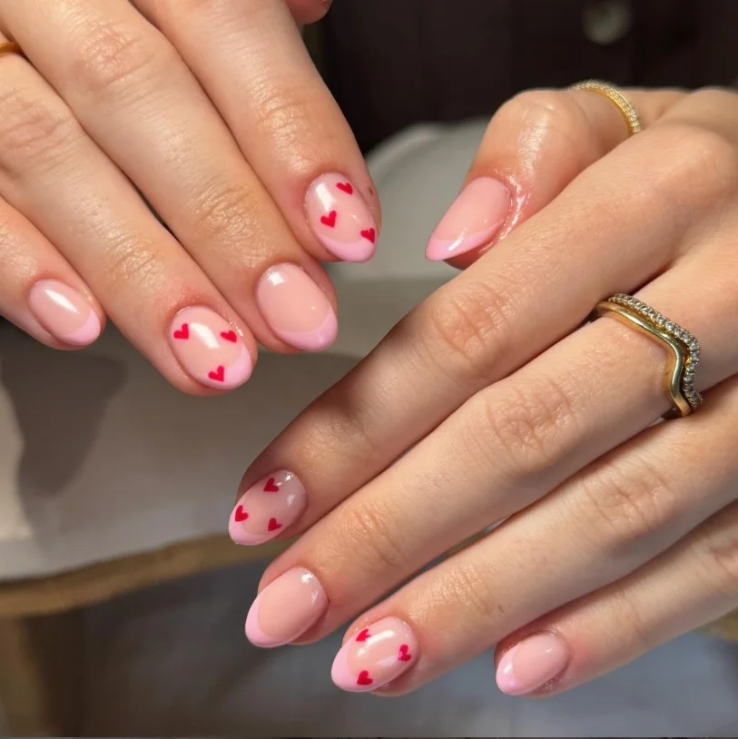 Cute pink French tip nail designs featuring tiny heart accents on a natural glossy nude base.