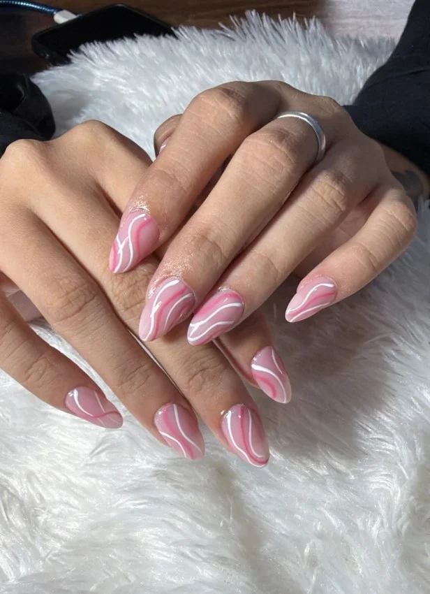 Pink and white swirl nail designs with flowing abstract line art on a glossy neutral base.