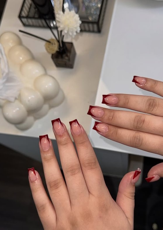 Red square nail designs featuring sharp V-cut French tips on a glossy nude foundation.