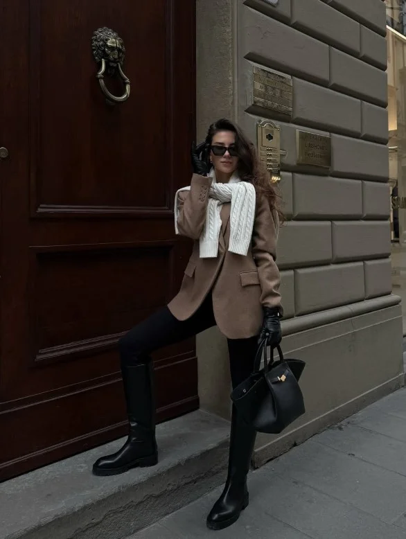 Woman wearing black knee-high boots with black jeans and a blazer.