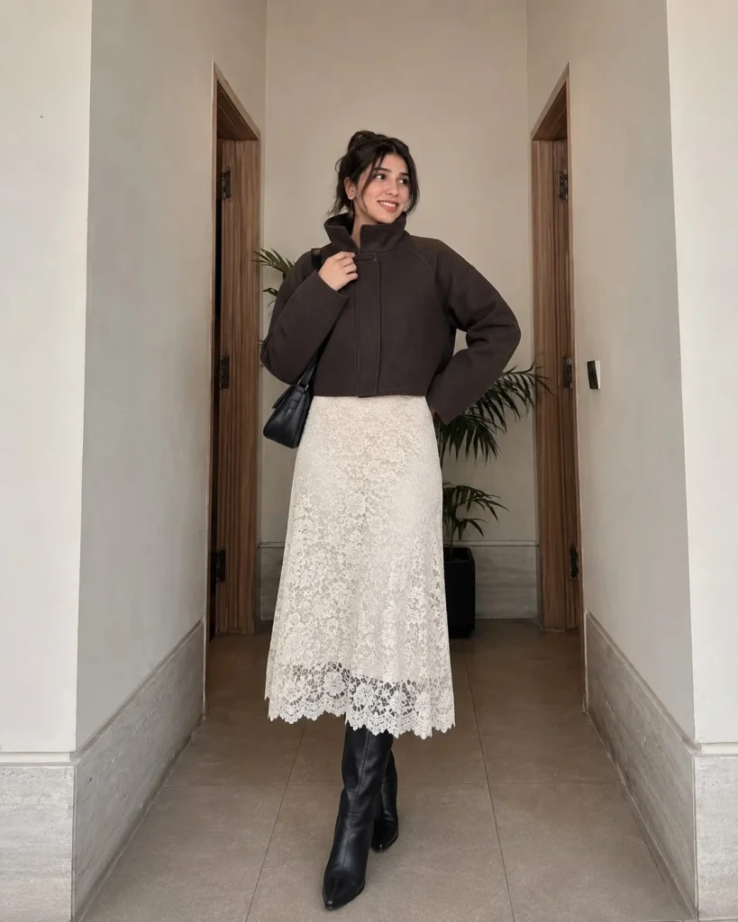 Woman wearing black knee-high boots with a lace-trim skirt and a funnel-neck jacket.
