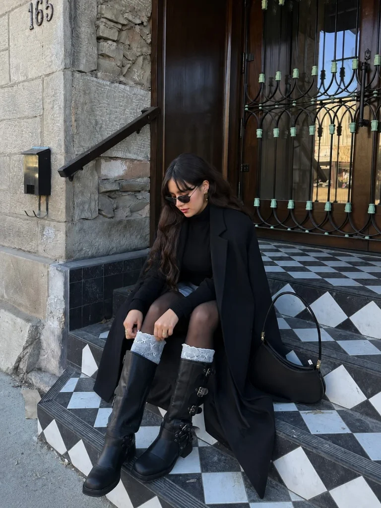 Woman wearing black knee-high boots with a mini skirt, black tights, and a long coat.