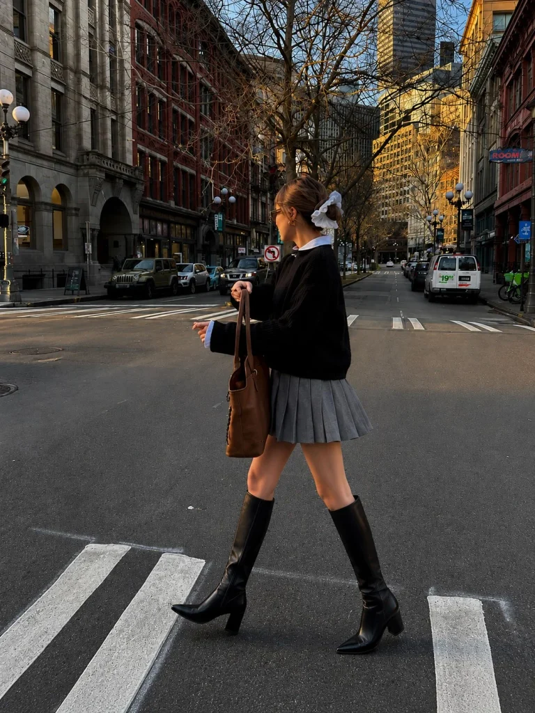 Woman wearing black knee-high boots with a pleated mini skirt and a fitted sweater.