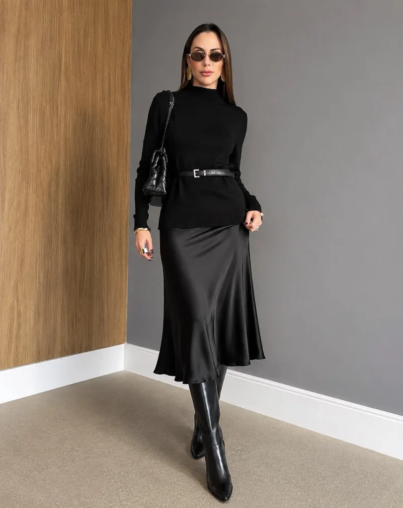 Woman wearing black knee-high boots with a satin midi skirt and a fitted knit sweater.