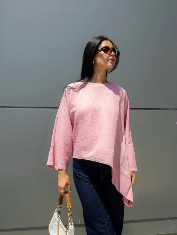 Woman wearing dark blue straight-leg jeans with a blush pink blouse, nude shoes, and a small handbag.