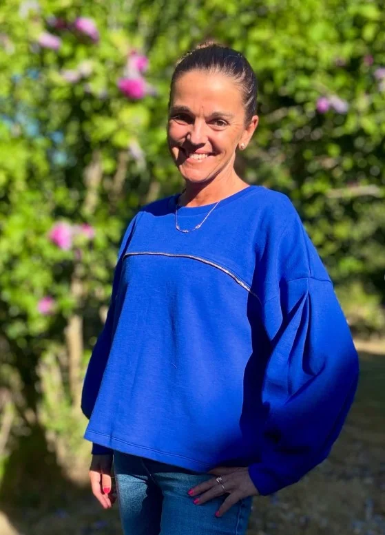 Woman wearing dark blue jeans with a bright cobalt blue top and simple neutral accessories.