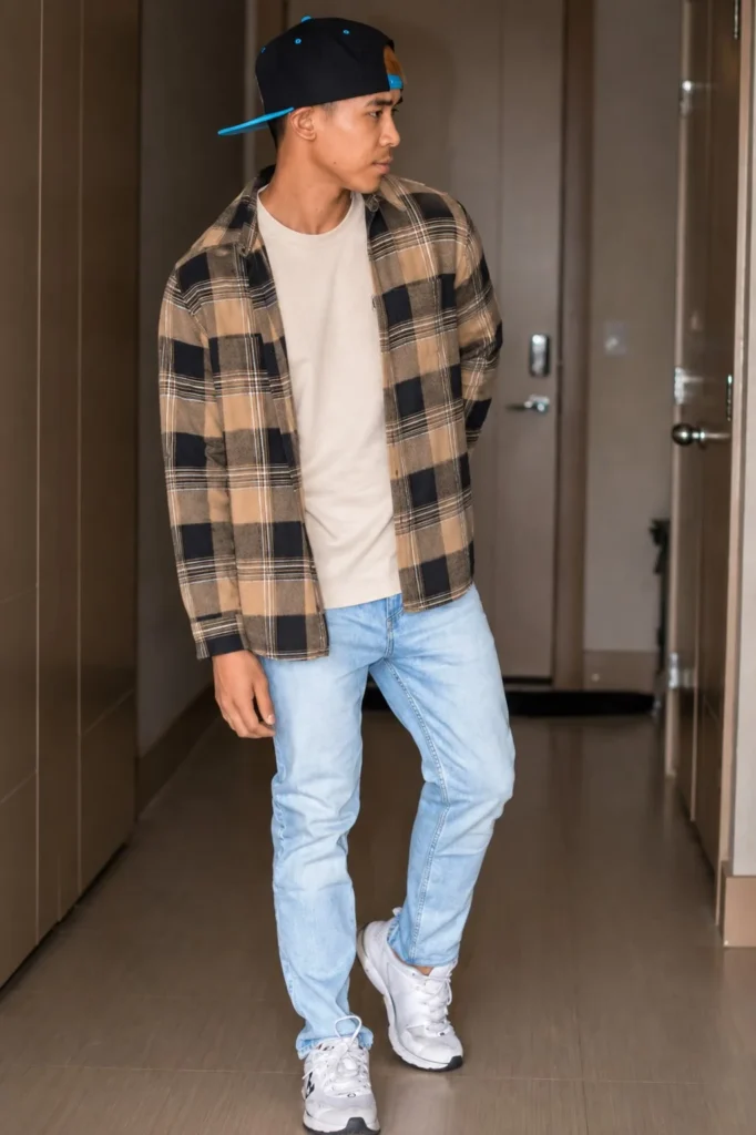 Man wearing an open brown plaid flannel over a cream T-shirt with dark jeans and suede boots.