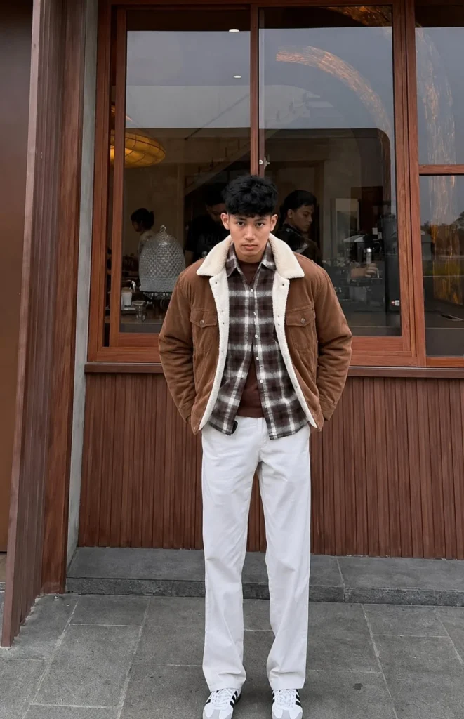 Man wearing a brown plaid flannel under a warm sherpa jacket with dark jeans and winter boots.
