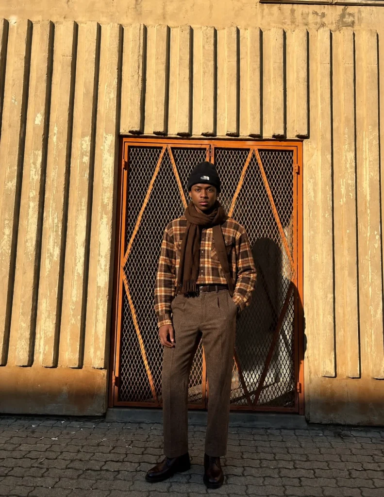 Man wearing a brown flannel with charcoal wool trousers, a winter scarf, and leather boots.