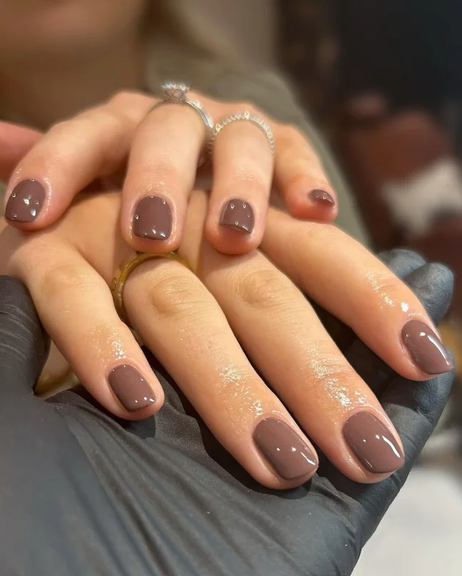 Glossy chocolate brown nail varnish creating warm rich contrast against pale skin.