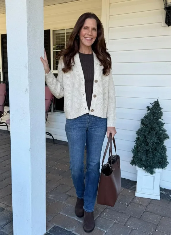 Woman wearing high-rise dark blue jeans with a cropped cream cardigan, ballet flats, and a small shoulder bag.