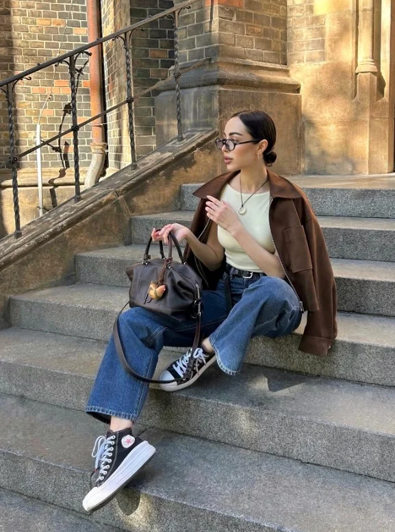 Woman wearing wide-leg dark blue jeans with a cropped structured jacket and sleek ankle boots.