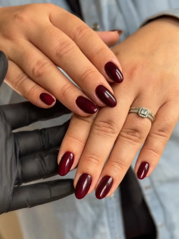 Deep burgundy nail varnish creating rich contrast against pale skin with a glossy finish.