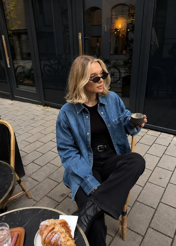 Woman wearing an open blue denim button-up shirt over a black top with black trousers.