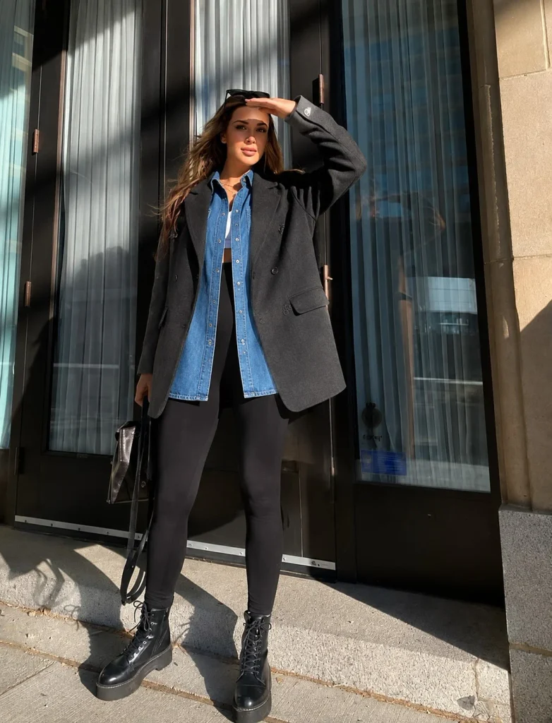 Woman wearing a blue denim button-up shirt with black leggings and an oversized black blazer.