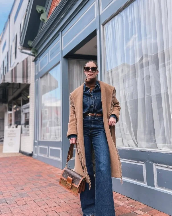 Woman wearing a blue denim button-up shirt with dark jeans and a camel coat.