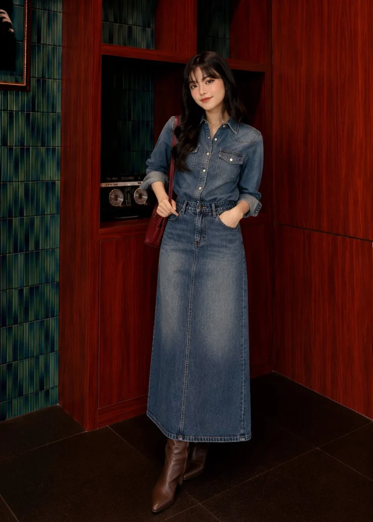 Woman wearing a blue denim button-up shirt with a long denim maxi skirt and knee-high boots.