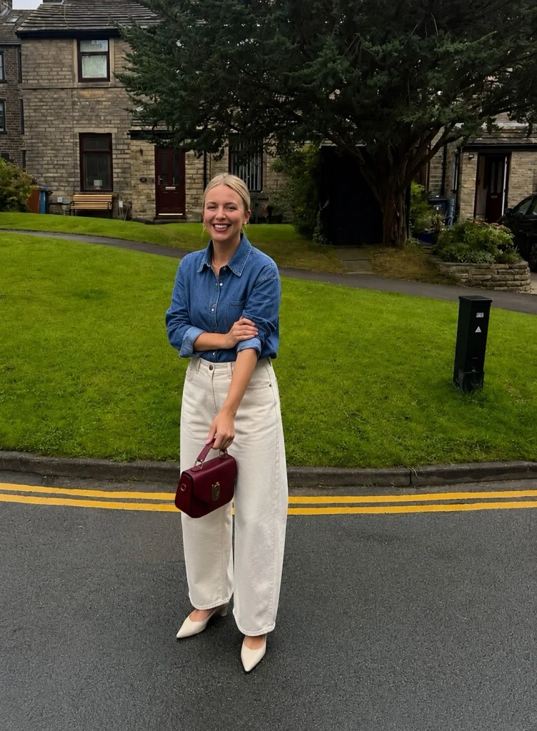 Woman wearing a blue denim button-up shirt with ecru barrel-leg jeans and pointed flats.