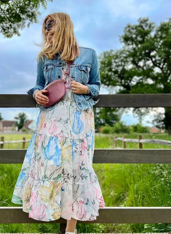 Woman wearing an open blue denim button-up shirt over a floral midi dress.