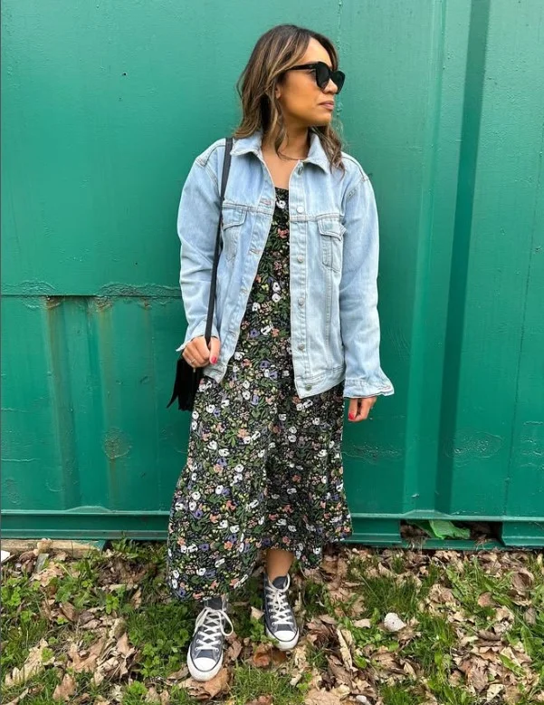 Woman wearing an open blue denim button-up shirt over a floral midi dress.
