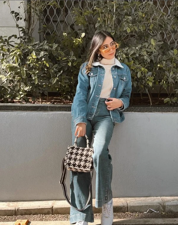 Woman wearing a blue denim button-up shirt over a cream turtleneck with dark trousers.
