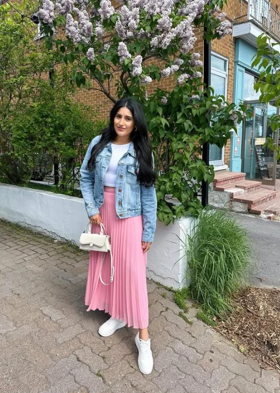 Woman wearing a blue denim button-up shirt with a charcoal pleated midi skirt.