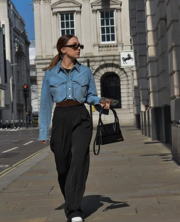 Woman wearing a blue denim button-up shirt with full-length pleated trousers and a slim belt.