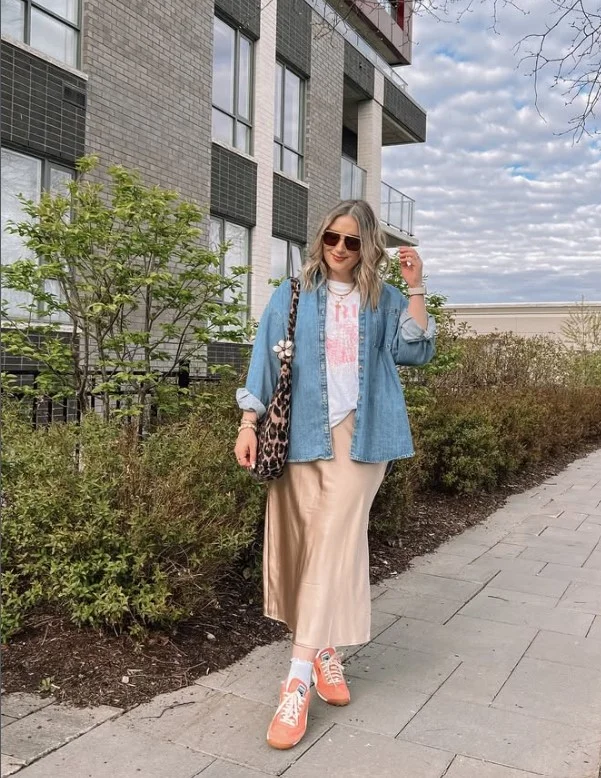 Woman wearing a blue denim button-up shirt with a black satin midi skirt.