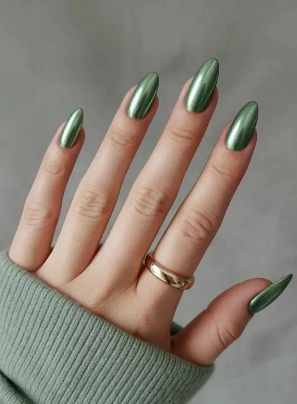 Rich emerald green nail varnish creating bold jewel-tone contrast against pale skin.