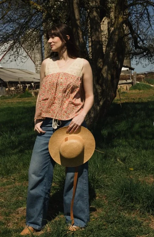 Woman wearing dark blue jeans with a floral blouse, pointed flats, and a small handbag.