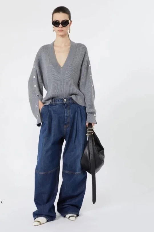 Woman styling dark blue jeans with a soft gray knit sweater, loafers, and a structured handbag.
