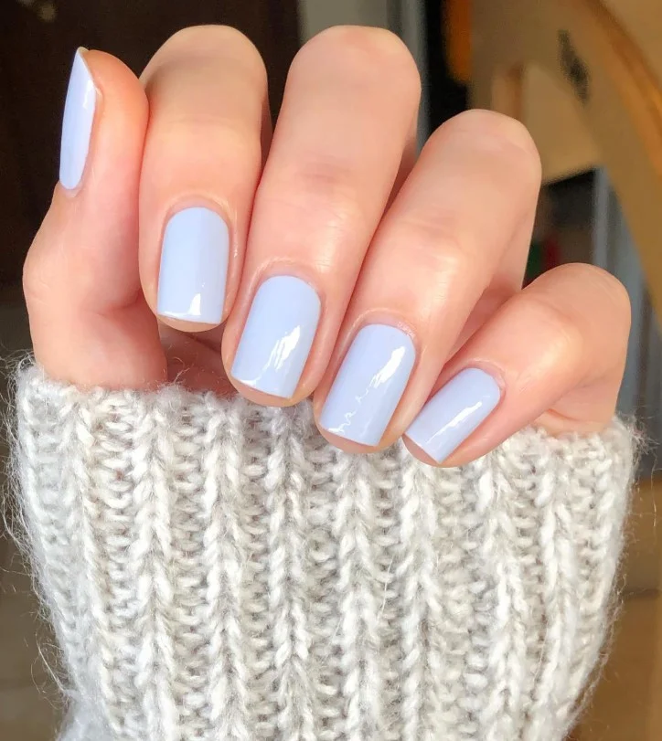 Icy blue nail varnish on pale skin creating a fresh cool-toned manicure with glossy shine.