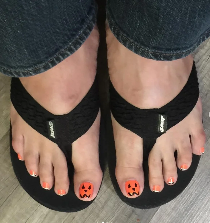 Jack-o’-lantern Halloween toe nail designs with tiny pumpkin faces on orange toenails.