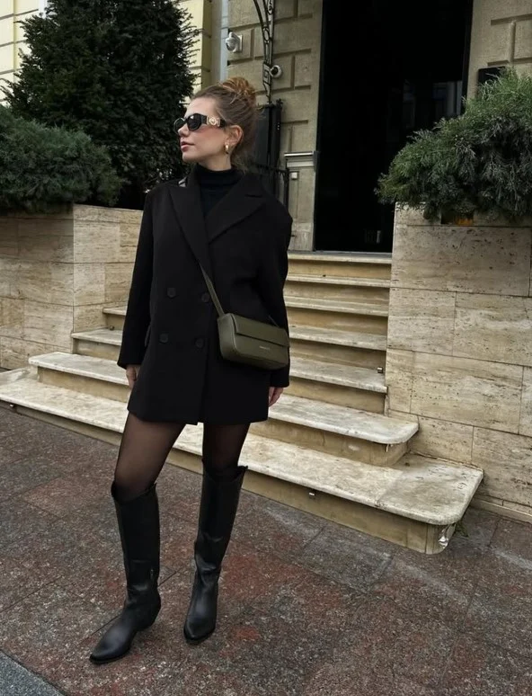 Woman wearing an all-black winter outfit with long black boots and layered black clothing