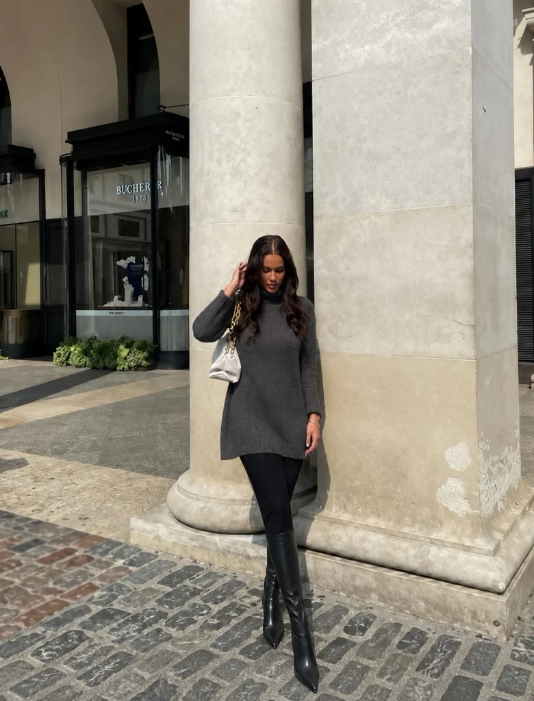 Woman wearing black leggings, a longline sweater, and long black boots